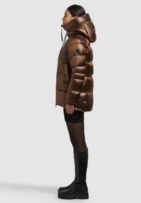 Brūna pūtēja jaka ar kapuci, spīdīga apdare, rūtainas šūšanas dizains, priekšējā rāvējslēdzēja un rāvējslēdzēja kabatas. Valkāta kopā ar melnu adītu svārku un garajiem zābakiem.