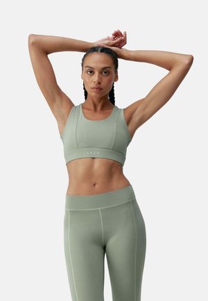 Lys grønn sports-BH og matchende leggings laget av glatt, elastisk stoff. BH-en har en bred kant og minimale sømdetaljer for komfort.