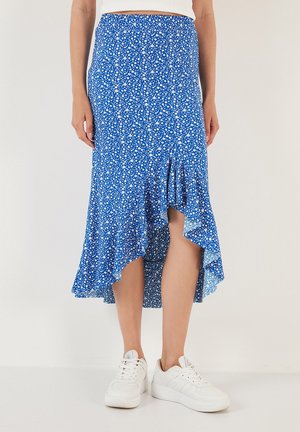 Gonna midi floreale blu con orlo asimmetrico, bordi arricciati e un tessuto leggero. Abbinata a sneakers bianche.