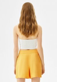 Top blanco corto con espalda texturizada y pantalones cortos de cintura alta naranjas. La tela parece suave, sin patrones ni adornos visibles.