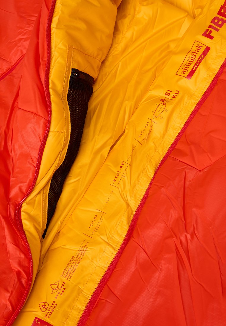 Saco de dormir en rojo brillante y amarillo con una textura suave y ripstop. Presenta un cierre con cremallera y un bolsillo de malla interior con detalles de aislamiento etiquetados.
