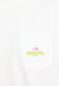 T-shirt en coton blanc avec une poche poitrine. Logo en rose et vert : "THE NORTH FACE" au-dessus de "EXPEDITION SERIES" dans une police de style graffiti.