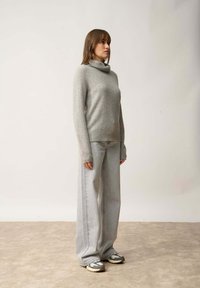 Szary, miękki sweter z golfem w połączeniu z jasnoszarymi spodniami o szerokich nogawkach. Modelka nosi masywne, wzorzyste sneakersy. Prosty, minimalistyczny design.