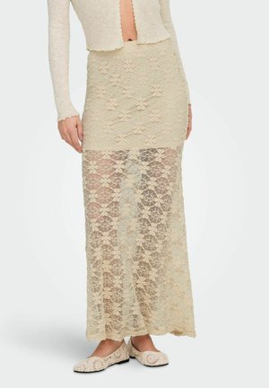 Beige maxi skjørt i blomsterblonder med ensfarget fôr til midt på låret, brukt sammen med matchende strikket kremhvit topp og slip-on sko i heklet stil.