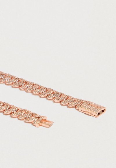 Náramek z růžového zlata s překlápěcím zapínáním, skládající se z článků ve tvaru listů osázených malými třpytivými krystaly, položený otevřený na bílém povrchu.