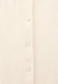 Zbliżenie beżowej siatkowej tkaniny z pionowym paskiem i trzema małymi pasującymi guzikami na środku.