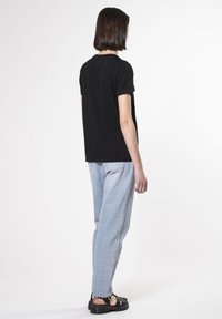 Camiseta de algodón negra de manga corta, combinada con jeans de mezclilla azul claro. El conjunto presenta un ajuste relajado y un detalle mínimo.