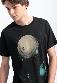 Zwarte katoenen t-shirt met een grafisch ontwerp van een planeet met ringen, kleine planeten en een figuur met vleugels, allemaal in gedempte kleuren en een kosmisch thema.