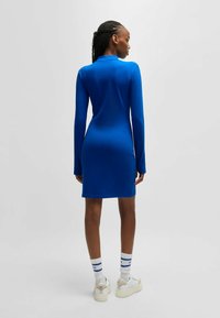 Langsleeve, bodycon jurk in een levendige blauwe stof, knielang ontwerp, gladde textuur, gecombineerd met witte sokken en platform sneakers.