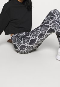 Felpa nera tagliata accoppiata con leggings attillati caratterizzati da un motivo a pelle di serpente bianco e nero. I leggings hanno una texture liscia e un design che valorizza la figura.