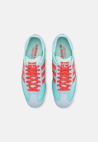 Adidas-sneakers med en turkos ovandel, röda ränder och snörning. Sämre accenter i ljusblått. Texturerad foder och varumärke på tungan.