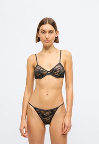 Conjunto de sutiã e fio dental em renda preta com alças ajustáveis e padrão floral. Tecido transparente com um acabamento suave e design minimalista.