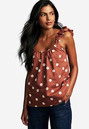 Top in tessuto con pois marroni, dotato di dettagli arricciati sulle spalle, scollatura elastica e tessuto morbido, abbinato a jeans di denim blu scuro.