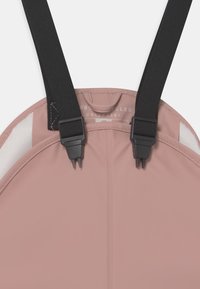Returpolyesterplagg med en myk rosa base og justerbare sorte stropper med plastklips, designet med en jevn tekstur og minimalistisk design.