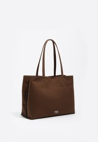 Ruda perčių maišelė su dviem ilgais rankenėlėmis, pagaminta iš lygaus sukimo, turi minimalų siuvimą ir logotipą apatinėje priekinėje dalyje.