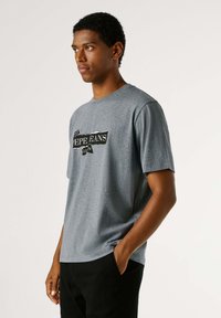 Sivé bavlnené tričko s krátkymi rukávmi, ktoré má na prednej strane čiernobielu grafickú potlač, okrúhly výstrih a voľný strih.