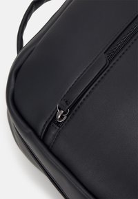 Sac en cuir synthétique noir avec une texture lisse, doté d'une fermeture éclair et d'un design élégant et arrondi. Agrémenté qu'accessoires en acier inoxydable.