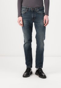 Sötétkék farmernadrág, slim fit szabású, öt zsebbel, gombos és cipzáras záródással, valamint finom fakulással a lábakon.