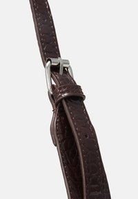 Tummanruskea nahkaranneke, jolla on suomumainen tekstuuri, ja hopeiset metalliosat sekä säädettävä solki.