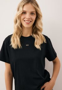 Czarny bawełniany t-shirt o swobodnym kroju, z krótkimi rękawami i małym złotym akcentem na klatce piersiowej. Gładka tekstura, minimalistyczny design.