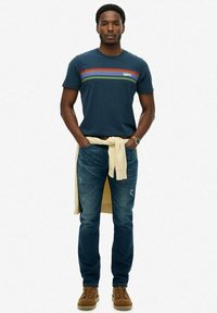 Mørkeblå bomulds t-shirt med vandrette flerfarvede striber, parret med lyseblå slidte jeans og brune snørebåndsstøvler. Sweater bundet om livet.