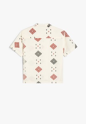 Kortærmet skjorte lavet af let tekstureret cremefarvet stof, med et geometrisk mønster af røde og sorte diamanter med krydser.