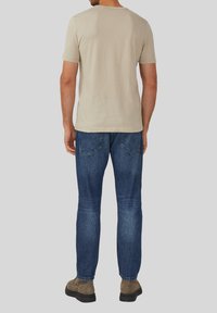 Beige shirt met korte mouwen gecombineerd met blauwe jeans. Het shirt heeft een ronde halslijn en de jeans hebben achterzakken met een vervaagde textuur.