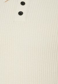 Tissu tricoté côtelé de couleur crème avec deux boutons noirs alignés verticalement près du centre supérieur.