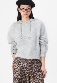 Ljusgrå, fluffig tröja med huva, med silverdetaljer och dragskor, i kombination med byxor med djurmönster och hög midja.