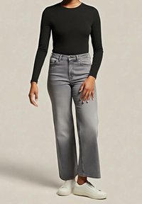 Jean gris à jambes larges et taille haute, associé à un haut noir ajusté à manches longues. Des baskets blanches complètent la tenue. Texture lisse partout.