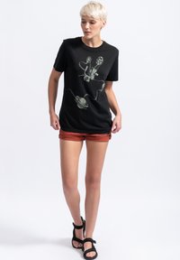 Zwarte katoenen t-shirt met een grafische print van een filmprojector en een planeet. Gecombineerd met glanzende roestkleurige shorts en zwarte sandalen.