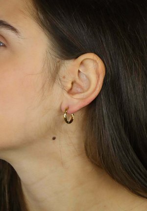 Pendiente de aro de oro con diseño retorcido, superficie texturizada y tamaño mediano, colocado sobre un fondo de cabello largo y oscuro.