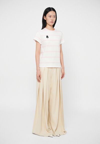 Camiseta às riscas, de manga curta, rosa e branca, com decote redondo e uma pequena graphic preta, combinada com calças largas de cor creme.