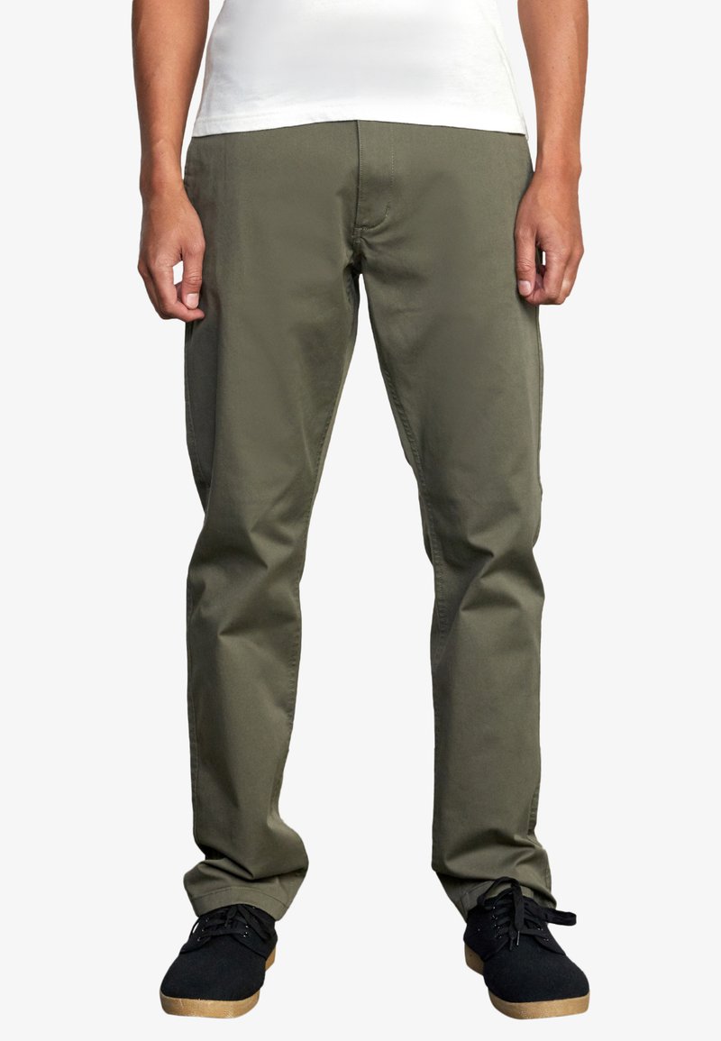 Olivgrüne, gerade geschnittene Hose aus Baumwollmischgewebe mit Fronttaschen und einem schlichten Bund, kombiniert mit schwarzen Sneakers.