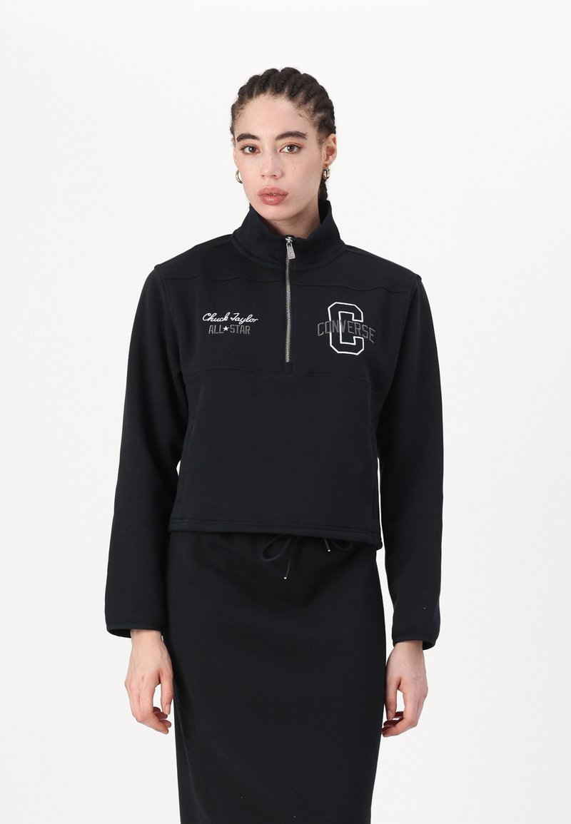 Sweatshirt cropped zippé noir avec col montant, présentant le logo blanc "Converse" et la broderie "Chuck Taylor ALL*STAR" sur le devant.