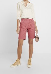 Shorts en coton rose avec une coupe droite et un ourlet retroussé, assortis à une chemise beige à manches longues et des baskets montantes couleur sable.