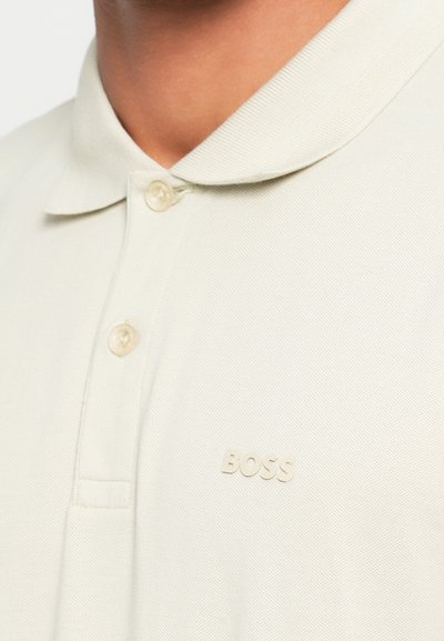 Polo beige avec un tissage texturé, doté d'un col classique, de deux boutons et d'un logo "BOSS" brodé discret sur la poitrine.