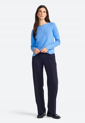 Maglia a maniche lunghe blu chiaro con scollo a barca, fessure laterali, abbinata a pantaloni blu navy scuri. Il tessuto sembra morbido con una finitura leggermente texturizzata.