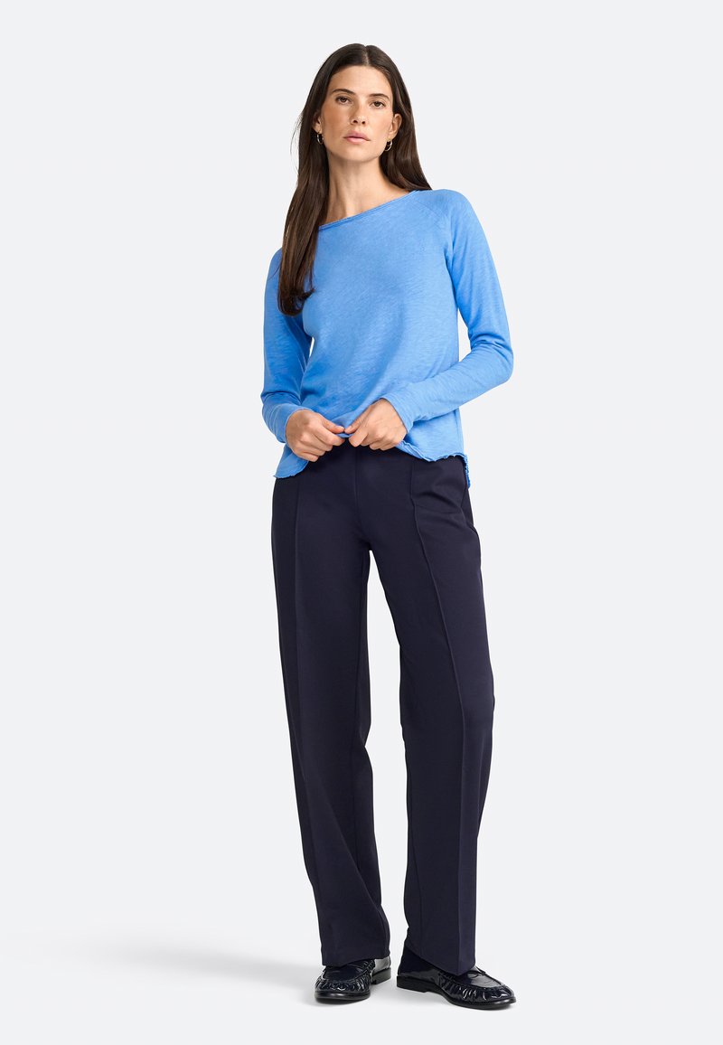Maglia a maniche lunghe blu chiaro con scollo a barca, fessure laterali, abbinata a pantaloni blu navy scuri. Il tessuto sembra morbido con una finitura leggermente texturizzata.
