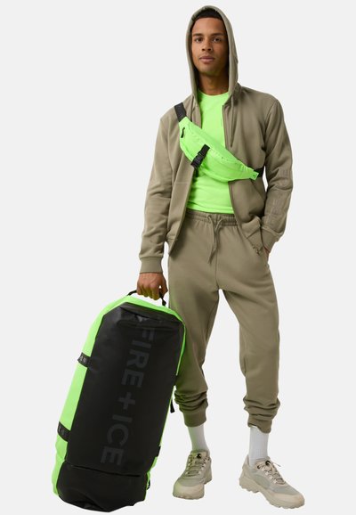 Zwarte en neon groene sporttas met de opdruk "FIRE + ICE", gecombineerd met een grijze trainingsoutfit, neon groene top en lichtgekleurde schoenen. Verstelbare schouderband.
