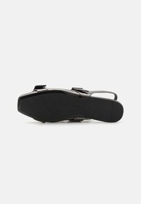 Zapato de charol negro con una textura suave, que cuenta con una suela plana y dos correas ajustables. La suela tiene un patrón de espiga para mayor agarre.