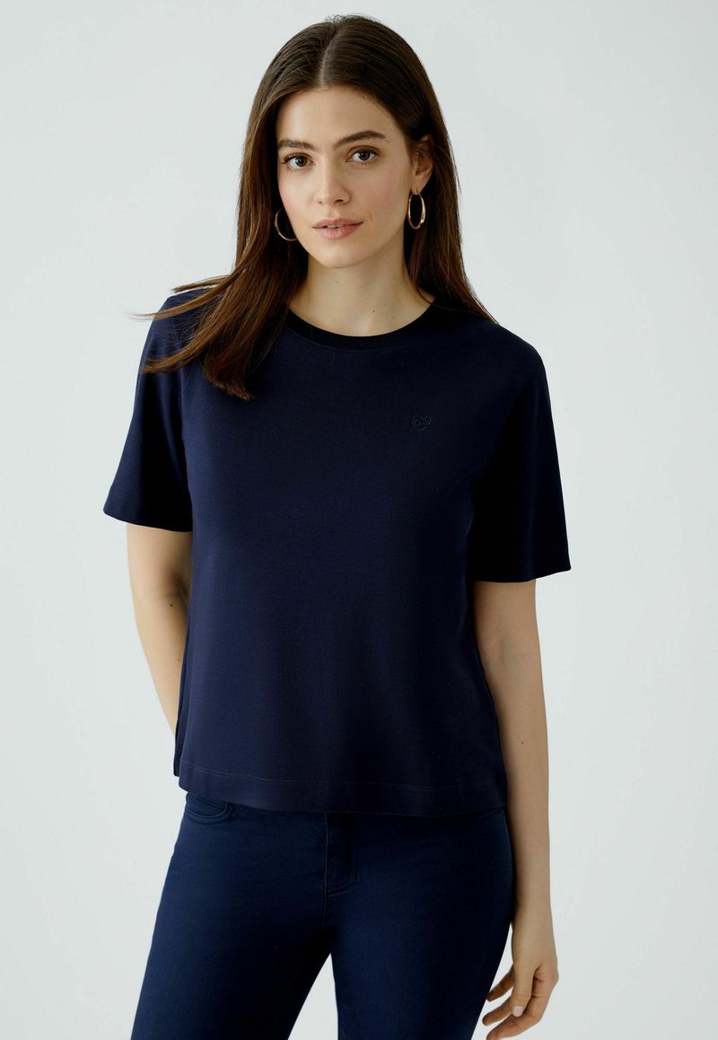 Navyblauwe t-shirt met korte mouwen in een aansluitende pasvorm, ronde halslijn en subtiele geborduurde logo op de borst. Soepele, zachte stof.