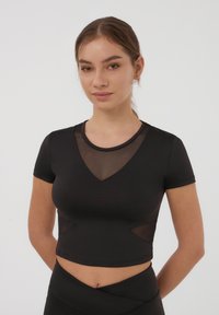 Top corto nero realizzato in un tessuto morbido, con pannelli in rete al colletto e sui lati, dotato di maniche corte e un design attillato.