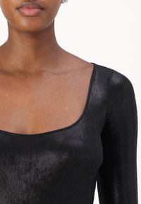 Top nero a maniche lunghe con scollatura ampia, realizzato in un tessuto liscio e lucido, caratterizzato da una finitura leggermente texturizzata.