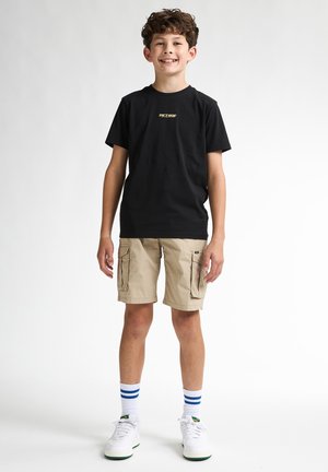 Czarny bawełniany t-shirt z złotym logo, beżowe spodenki cargo z kieszeniami, białe sneakersy z zielonymi akcentami oraz skarpetki w niebieskie paski.