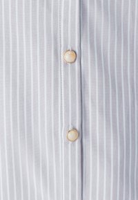 Gestreiftes Shirt in Grau und Weiß mit glattem Stoff, klassischem Kragen und runden Knöpfen mit goldenem Rand und hellfarbigem Zentrum.