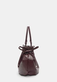 Ciemnobrązowa skórzana torebka z podwójnymi uchwytami i zaciąganym zamknięciem sznurkowym, widziana z boku na białym tle.