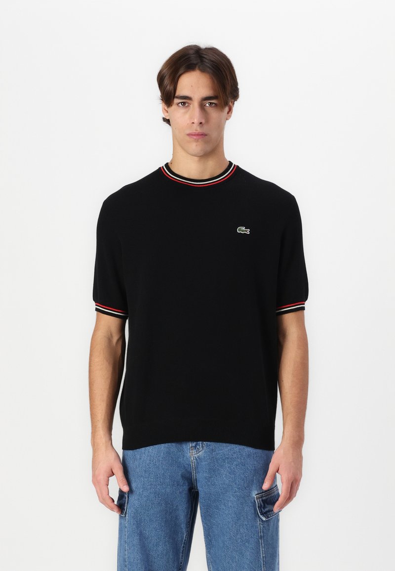 Black short-sleeve sweater with red and white striped ribbed collar and cuffs. Features a Lacoste logo on the chest. Smooth texture.