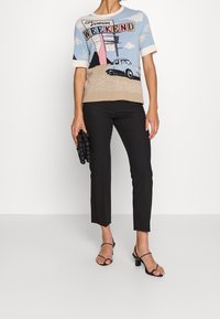 Gebreide trui in blauw, beige en wit met een retro autografiek en de tekst "Fantasy WEEKEND." Zwarte slim-fit broek en zwarte sandalen.