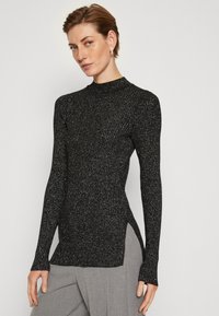 Svart ribbad långärmad topp med hög krage. Har metalltråd för glitter, sidofickor och en figurnära design. Slät textur.